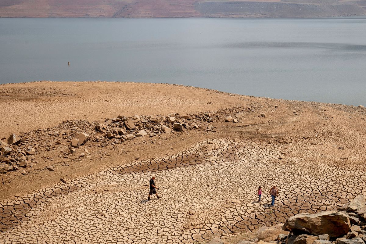 A family walks over cracked mud near Lake Oroville’s shore on Aug. 22, 2021, as water levels remain low due to continuing drought conditions in Oroville, Calif. State water officials are preparing to tell urban and agricultural water agencies on Friday they’ll get even less water from state supplies than the small amount they were promised at the start of the year. Lake Oroville is currently 68% of its historical average supply. (Ethan Swope)