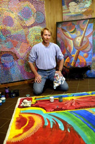 Gregg Perrenoud and cat Amber in his Greenacres studio with three paintings in various stages. Perrenoud, a longtime Spokane area resident, paints brightly-colored abstract pieces like
