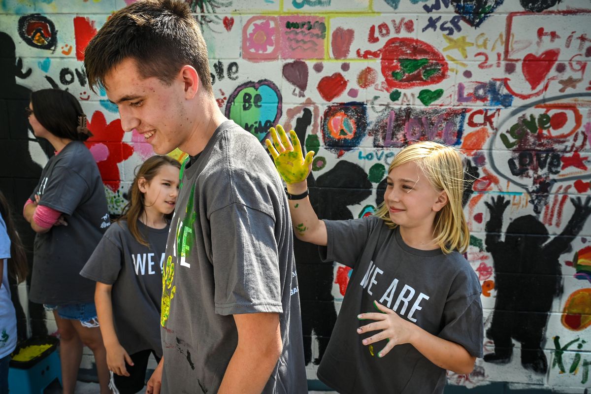 Westview Elementary School third grader Blake Heller adds his painted handprint to the shirt of Shadle Park Leadership Class member Egan Johnson as they create a mural on a building n an alley near the corner of Monroe Street and Garland Avenue, Friday, June 16, 2023, in Spokane