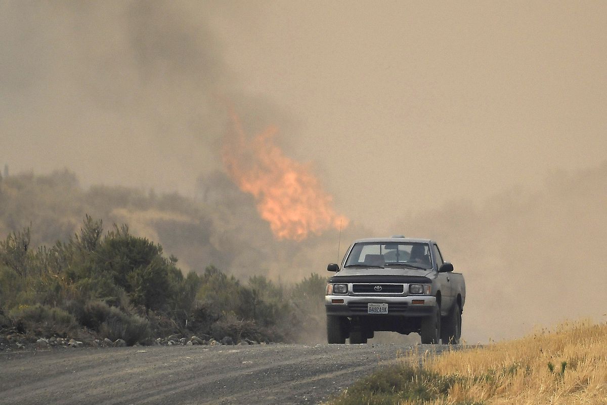 A pickup drives down a dirt road as the Pearl Hill Fire’s flames ignite behind it on Tuesday, Sept. 8, 2020, near Mansfield, Wash.  (Tyler Tjomsland / The Spokesman-Review)