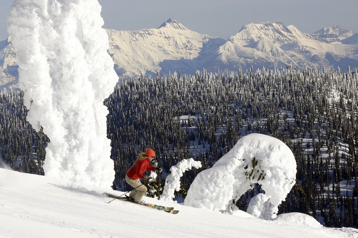 A skier near the summit of Big Mountain at Whitefish Mountain Resort in Montana glides by the signature snow ghosts with the peaks of Glacier National Park in the background.  (Brian Schott / Associated Press)