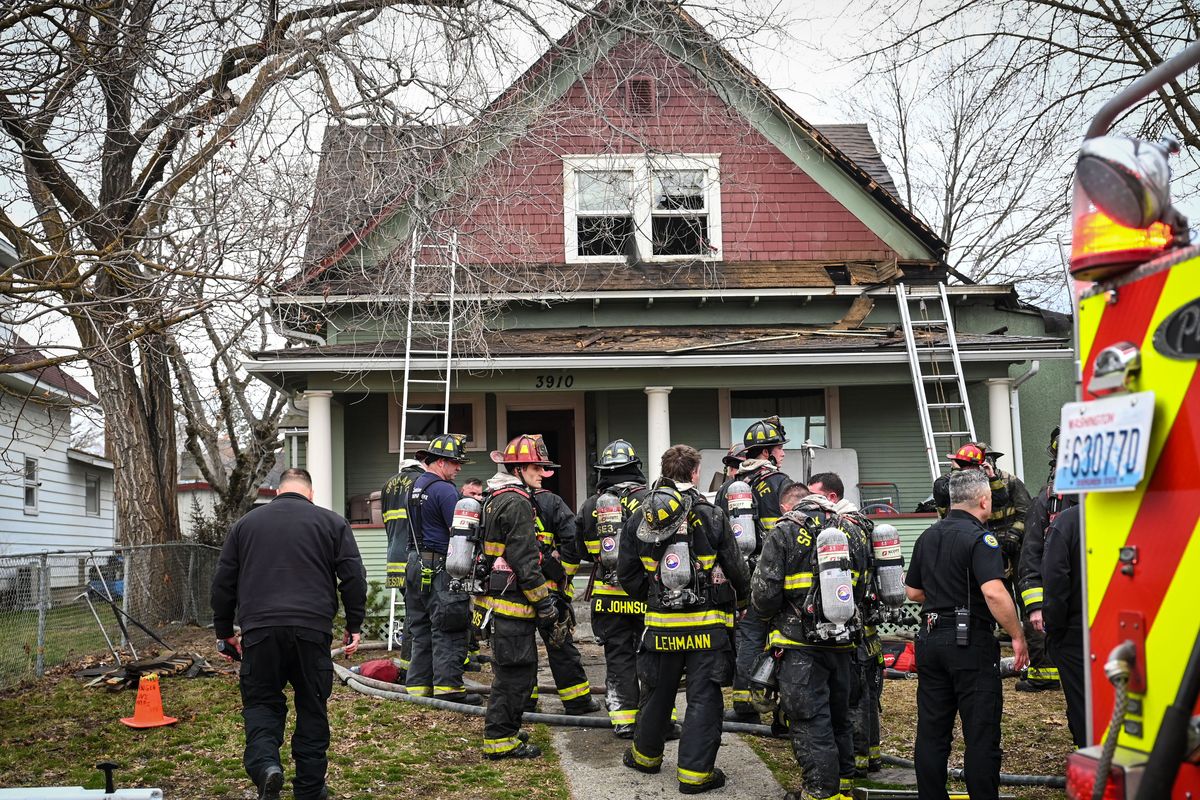 Spokane firefighters gather in the front yard after a suspicious blaze near the corner of Wall Street and Garland Avenue sent a woman to the hospital, Thursday, March 23, 2023, in Spokane. (DAN PELLE/THE SPOKESMAN-REVIEW)