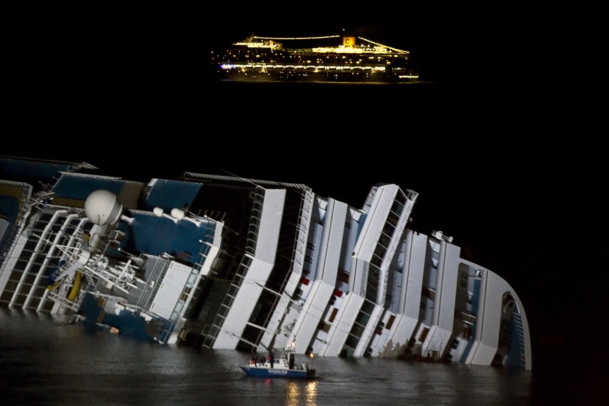 The cruise ship Costa Serena passes offshore as its sister ship Costa Concordia lies on its side off the tiny Tuscan island of Giglio, Italy, on Wednesday. (Associated Press)