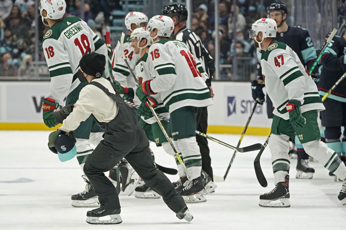 A worker picks up hats that were thrown onto the ice after a hat trick by Minnesota Wild center Rem Pitlick (16) against the Seattle Kraken during the second period of an NHL hockey game Saturday, Nov. 13, 2021, in Seattle.  (Ted S. Warren)