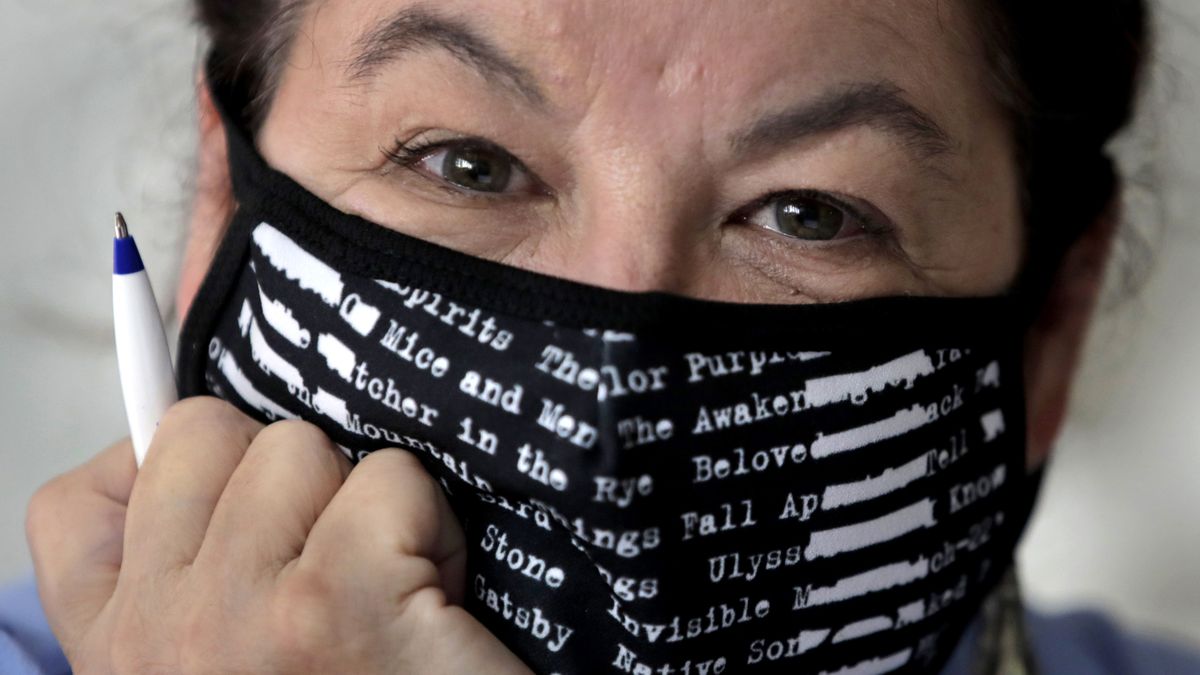Poet Tammi Truax poses at her writing table, wearing a protective mask due to the COVID-19 virus outbreak, Wednesday, July 29, 2020, at her home in Eliot, Maine. Truax, the poet laureate for Portsmouth, N.H., pens a weekly pandemic poem that is included in the city