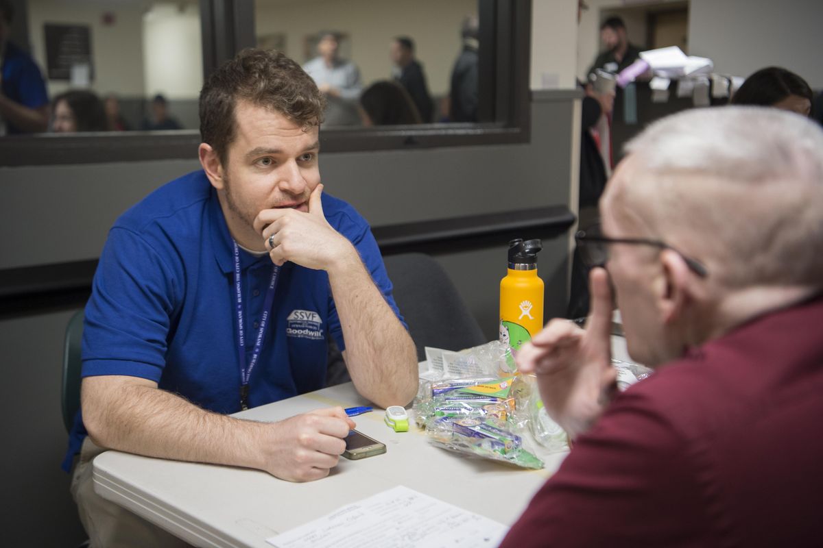 Josiah Torba, left, one of more than a hundred people involved in the counting process, interviews a man, right, who gave his name as Sharky in the dayroom of the Union Gospel Mission, Thursday, Jan. 25, 2018, during the annual count of homeless peopl across Spokane. Torba is using his smart phone to do the interview and numbers are uploaded in real time as surveys are completed. (Jesse Tinsley / The Spokesman-Review)