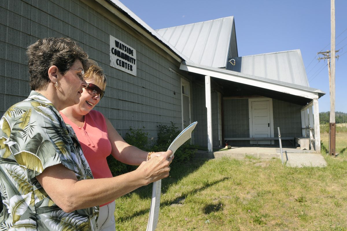Vonnie Hale, left, and Cherrie Massender look at a history book showing pictures of Montfort School, now called the Wayside Community Center, background, July 24. (Dan Pelle / The Spokesman-Review)