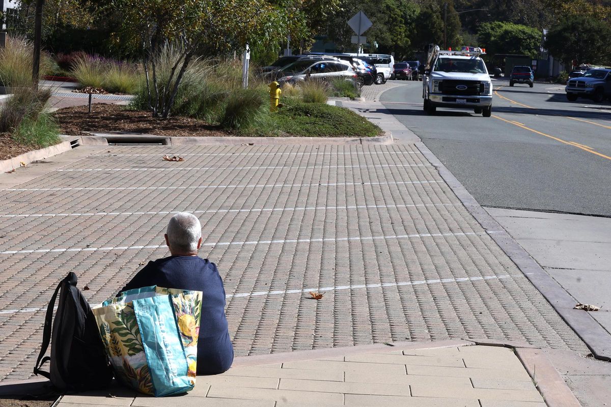 A homeless woman sits with her belongs across the street from Legacy Park, where a handful of homeless people live in Malibu, California on Oct. 15, 2025. (Genaro Molina/Los Angeles Times/TNS)