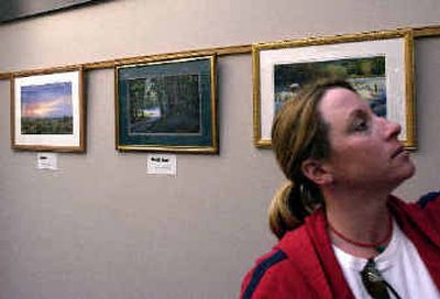 
Lisa Slarks peruses the audio-visual selections in the Valley branch of the library Monday. The paintings behind her are, from left, Sunset, Woods Road and Winter Embrace, all by Susan Rohrback. 
 (Liz Kishimoto / The Spokesman-Review)