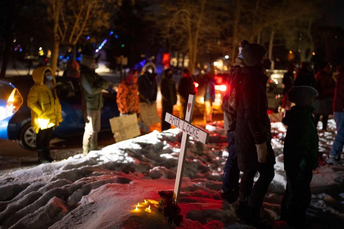 People stand by a cross planted in the boulevard outside homes at the intersection of and Dean Parkway and W. 28th St. in Minneapolis Sunday night, Feb. 6, 2022. At least 150 demonstrators in a caravan of dozens of cars gathered outside a home thought to be where Interim Minneapolis Police Chief Amelia Huffman resides on Dean Parkway to call for justice for Amir Locke, who was shot and killed by Minneapolis Police the previous week.  (Jeff Wheeler)