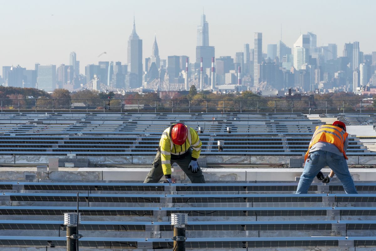 FILE - Framed by the Manhattan skyline electricians with IBEW Local 3 install solar panels on top of the Terminal B garage at LaGuardia Airport, Tuesday, Nov. 9, 2021, in the Queens borough of New York. As climate change pushes states in the U.S. to dramatically cut their use of fossil fuels, many are coming to the conclusion that solar, wind and other renewable power sources won