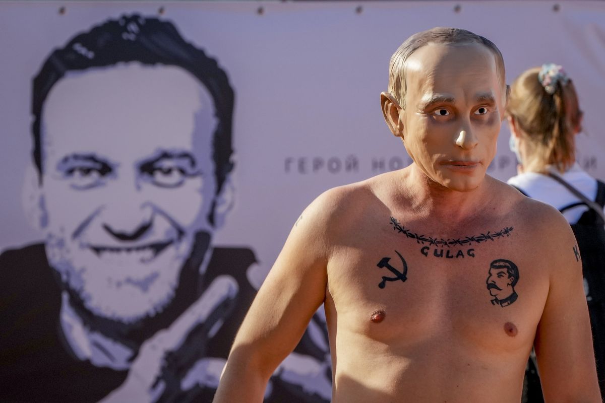 A man wearing a Vladimir Putin mask takes part in a demonstration for imprisoned Alexei Navalny, poster at left, in Geneva, Switzerland Tuesday, June 15, 2021. US President Joe Biden and Russia President Vladimir Putin will meet for talks in Geneva on Wednesday. (Michael Probst)