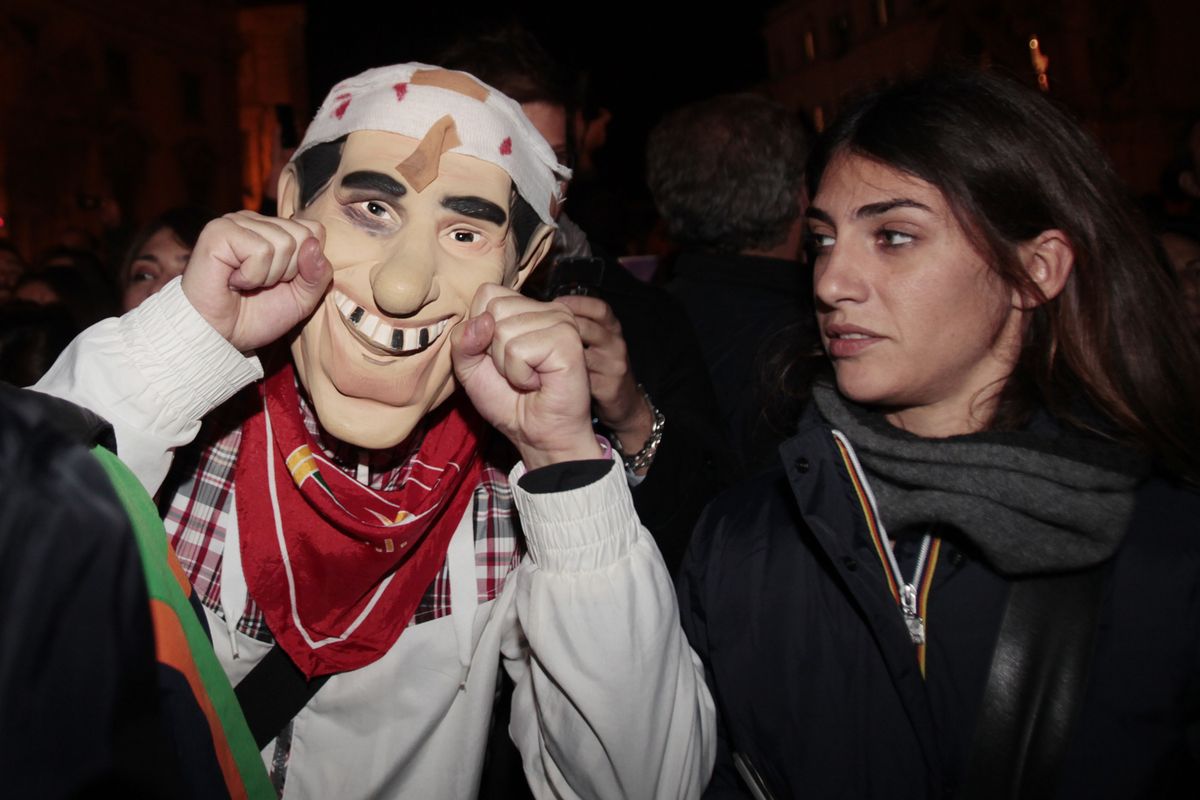 A man wearing a mock mask of Italian Premier Silvio Berlusconi celebrates outside Quirinale Presidential Palace in Rome on Saturday after news spread of Berlusconi’s resignation. (Associated Press)