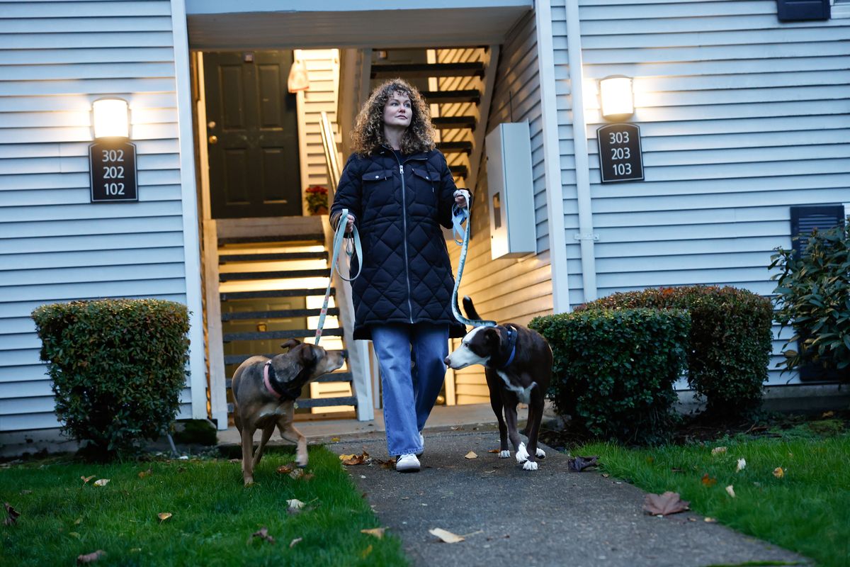 Jessica Poe photographed with her two dogs, Rango (black and white) and Bijou after she comes home from work at her apartment in Redmond, Washington, on Tuesday, Nov. 19, 2024. She moved from Spanaway to Redmond for a job that requires her to work in-person five days a week, but her commute is only 15 minutes instead of four hours and she can bring her dogs to work.   (Karen Ducey/The Seattle Times/TNS)