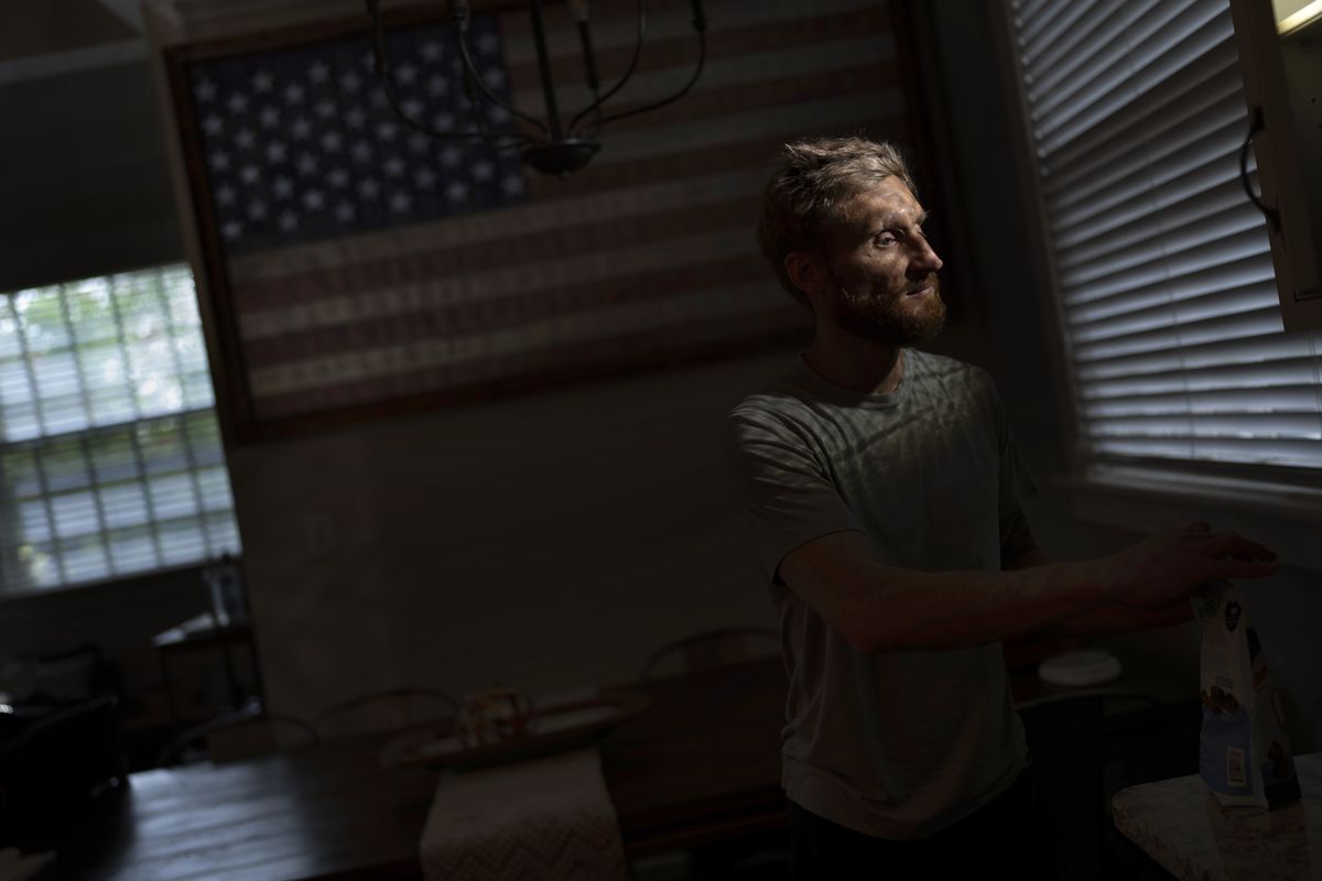 Brad Snyder prepares tea for his wife in their kitchen decorated with a flag handcrafted by Brooklyn firefighters using recycled firehose, in Princeton, N.J., on Wednesday, Aug. 4, 2021. Losing his sight, he says, seems to matter more to other people.  (Emilio Morenatti)