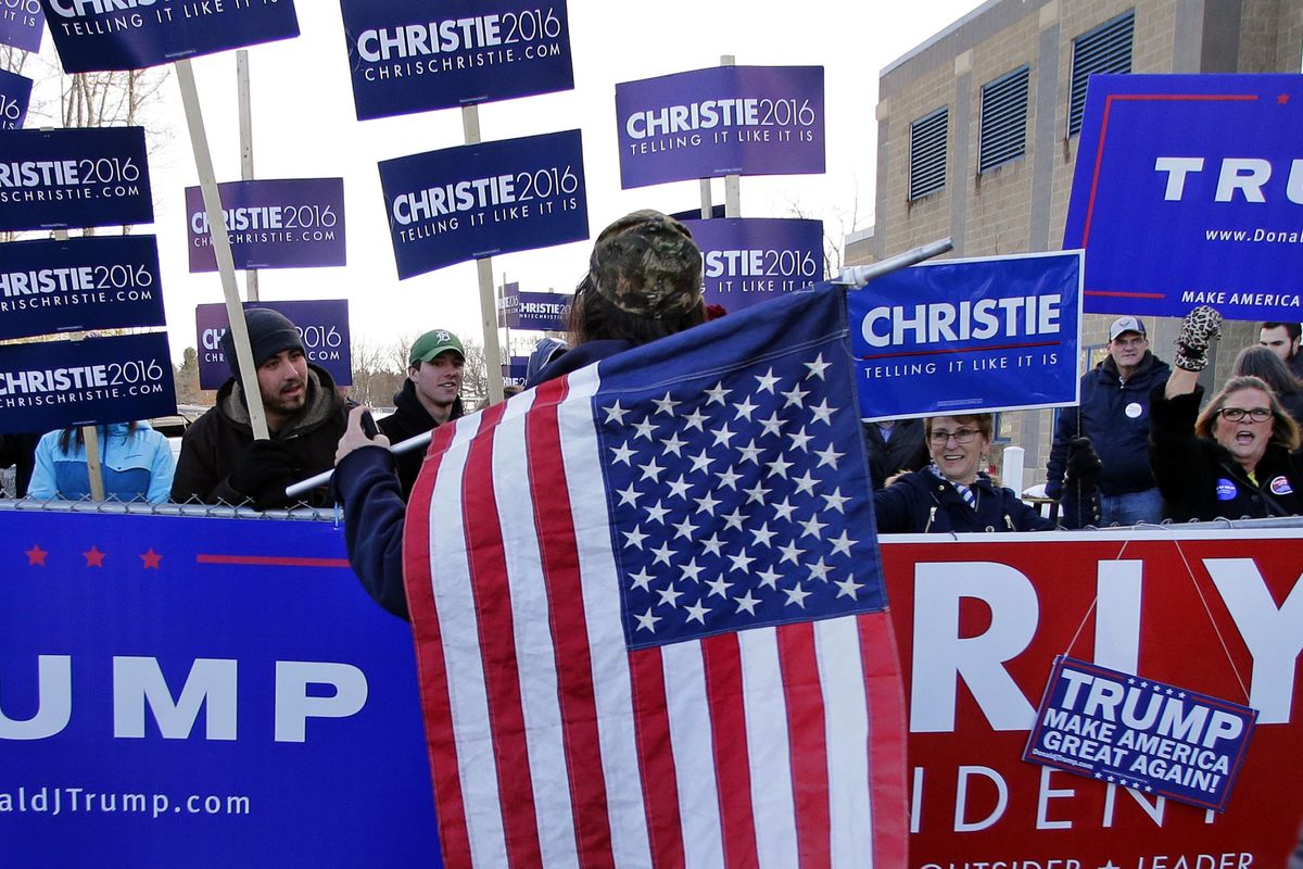 Rod Webber of Boston, holds an American flag as he talks with presidential candidate volunteers holding signs outside a polling station on primary day in Londonderry, N.H., Tuesday, Feb. 9, 2016. (Charles Krupa / Associated Press)
