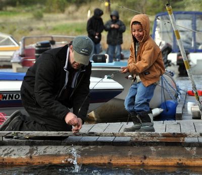Ted Urban of Spokane helps his nephew, Christopher Salinas, land his first fish on the docks at Fishtrap Lake Resort on Saturday, the opening day of Washington's trout fishing season.  (Rich Landers)