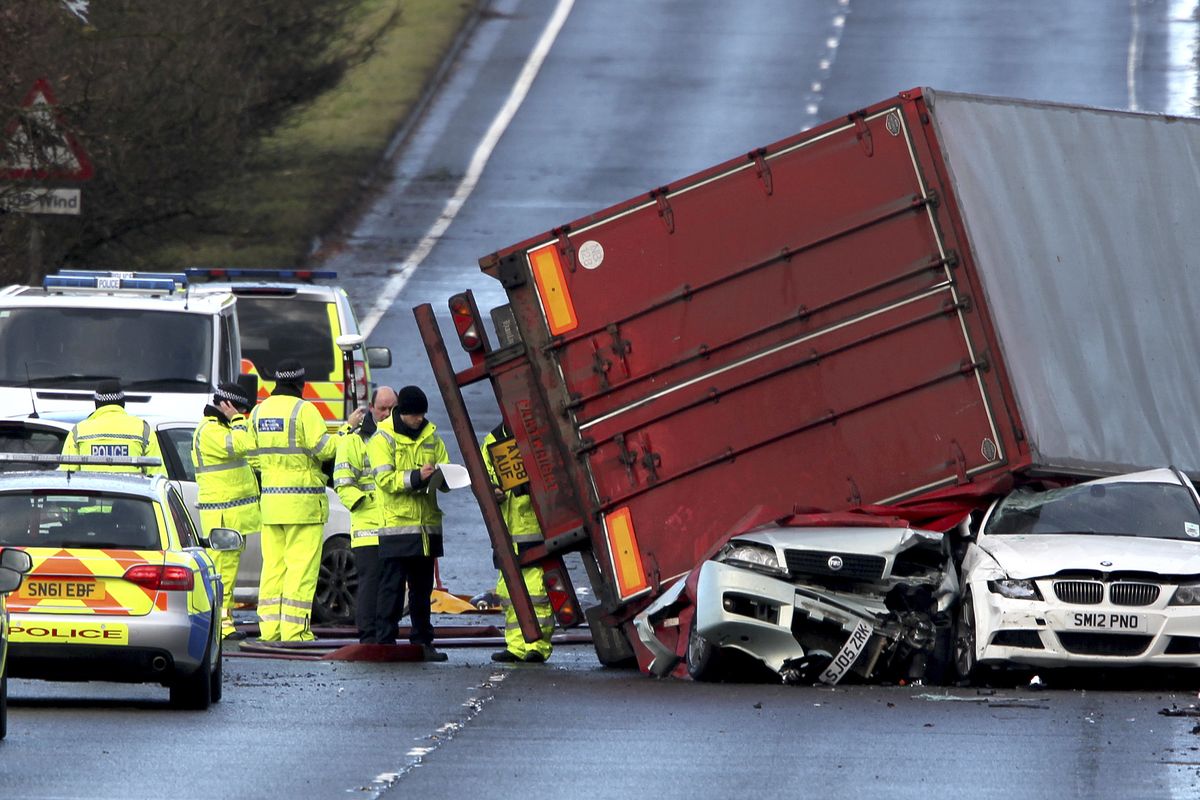 Emergency workers attend the scene of a fatal truck accident as a lorry sits on top of two cars near Bathgate, Scotland, after strong winds hit the region early Thursday. (Associated Press)