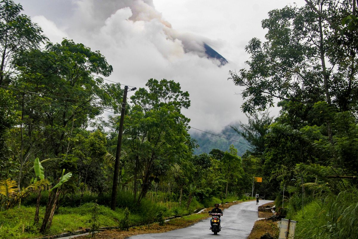 A resident rides a motorcycle past a street as Mount Merapi spews volcanic materials in the background, seen from Cangkringan village in Sleman, Yogyakarta, Thursday, March 10, 2022. Indonesia