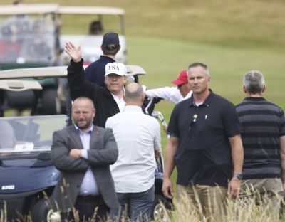 U.S. President Donald Trump waves to protesters while he plays golf at Turnberry golf club, Scotland, Saturday, July 14, 2018. Trump is spending the weekend at his seaside Trump Turnberry golf resort, where aides had said he would be busy preparing for his Monday summit in Helsinki, Finland. (Peter Morrison / Associated Press)