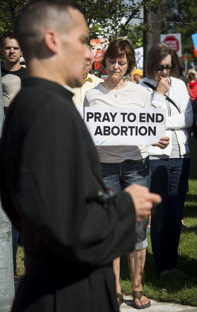 Father Dennis Gordon from St. Joan of Arc Chapel in Coeur d'Alene prays the rosary as Helen Machtolf, holding sign and others join in near the Spokane Planned Parenthood office on North Rudy Street. About 200 anti-abortion protestors picketed Spokane Planned Parenthood, Sat. Aug. 22, 2015. (Colin Mulvany)