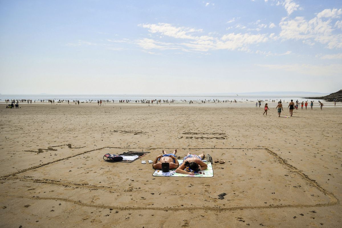 People sunbathe in a marked out square in the sand, indicating two meters, on Barry Island beach, in Wales, Friday, July 31, 2020. First Minister for Wales, Mark Drakeford, has announced that from Monday up to 30 people can meet outside while maintaining social distancing in the latest easing of coronavirus measures in Wales.  (Ben Birchall)