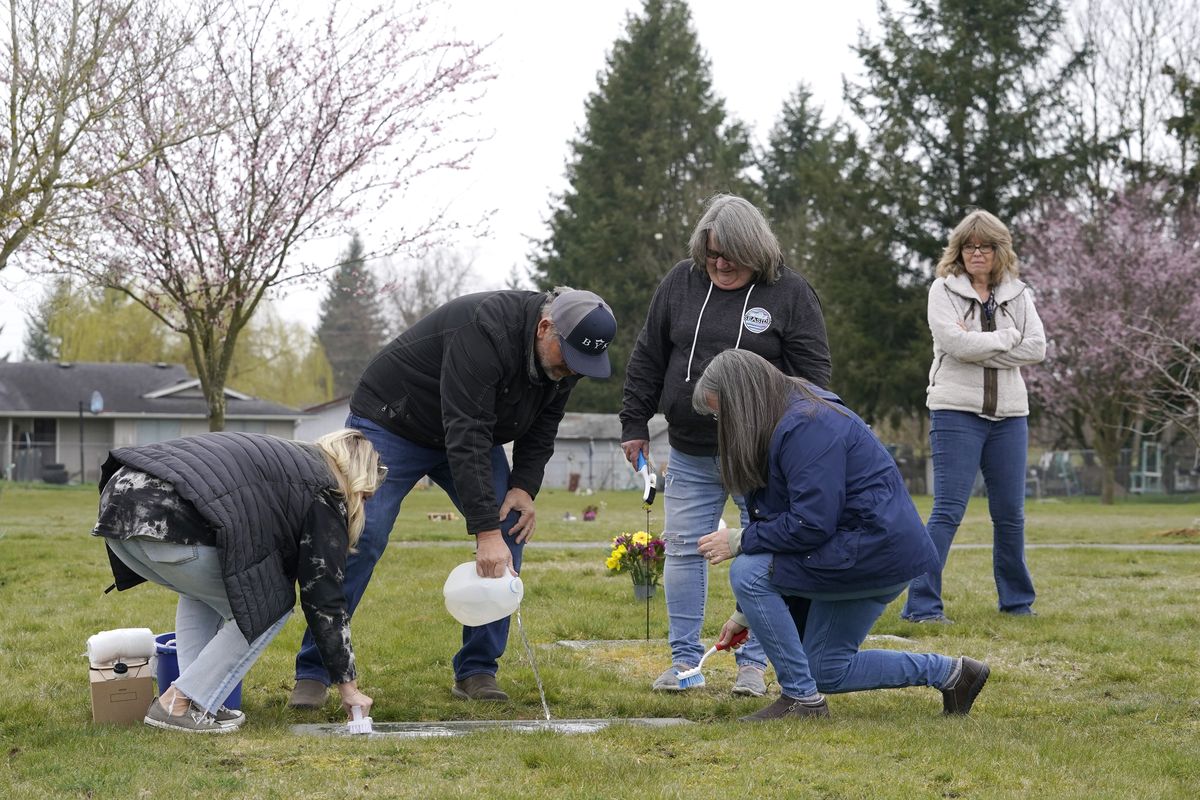 From front left, Wendy Jensen, Joe Woodmansee, Linda Holeman and Bonnie Dawson, the four children of Carole Rae Woodmansee, are joined by family friend Debbie Blazina, at right, Saturday, March 27, 2021, as they clean the headstone Carole shares with their father, Jim, who died in 2003, at Union Cemetery in Sedro-Woolley, Wash., north of Seattle, prior to a memorial service. Carole died a year ago on the same date in 2020, the day of her 81st birthday, from complications of COVID-19 after contracting it during a choir practice that sickened 53 people and killed two — a superspreader event that would become one of the most pivotal transmission episodes in understanding the virus.  (Ted S. Warren)