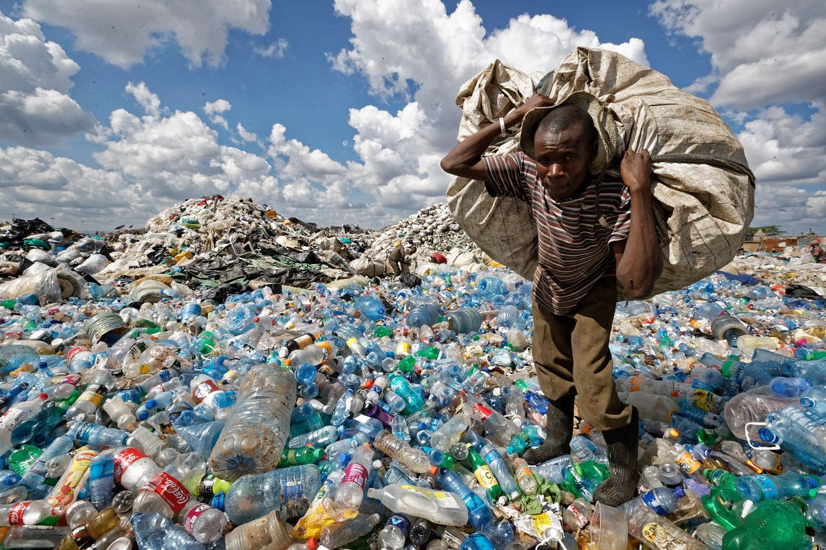 A man walks on a mountain of plastic bottles Dec. 5, 2018, as he carries a sack of them to be sold for recycling after weighing them at the dump in the Dandora slum of Nairobi, Kenya. The U.N. Environment Assembly, meeting Feb. 28 to March 2 in Nairobi, Kenya, is expected to propose an international framework to address plastic waste.  (Ben Curtis)