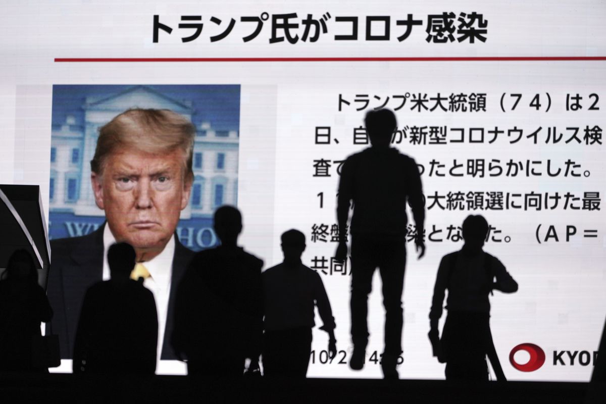 People walk past a screen showing the news report that President Donald Trump has tested positive for the coronavirus, Friday, Oct. 2, 2020, in Tokyo. President Trump said Friday that he and first lady Melania Trump have tested positive for the coronavirus, just a month before the presidential election and after having spent much of the last year largely downplaying the threat of the virus. (Eugene Hoshiko)