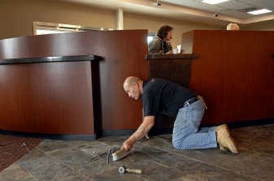 
James Sandbak  of Great Floors sweeps the debris off of the floor of the front lobby while customer service representative Besa Anderson works on the computer of the new Community 1st Bank in Post Falls. 
 (Kathy Plonka / The Spokesman-Review)