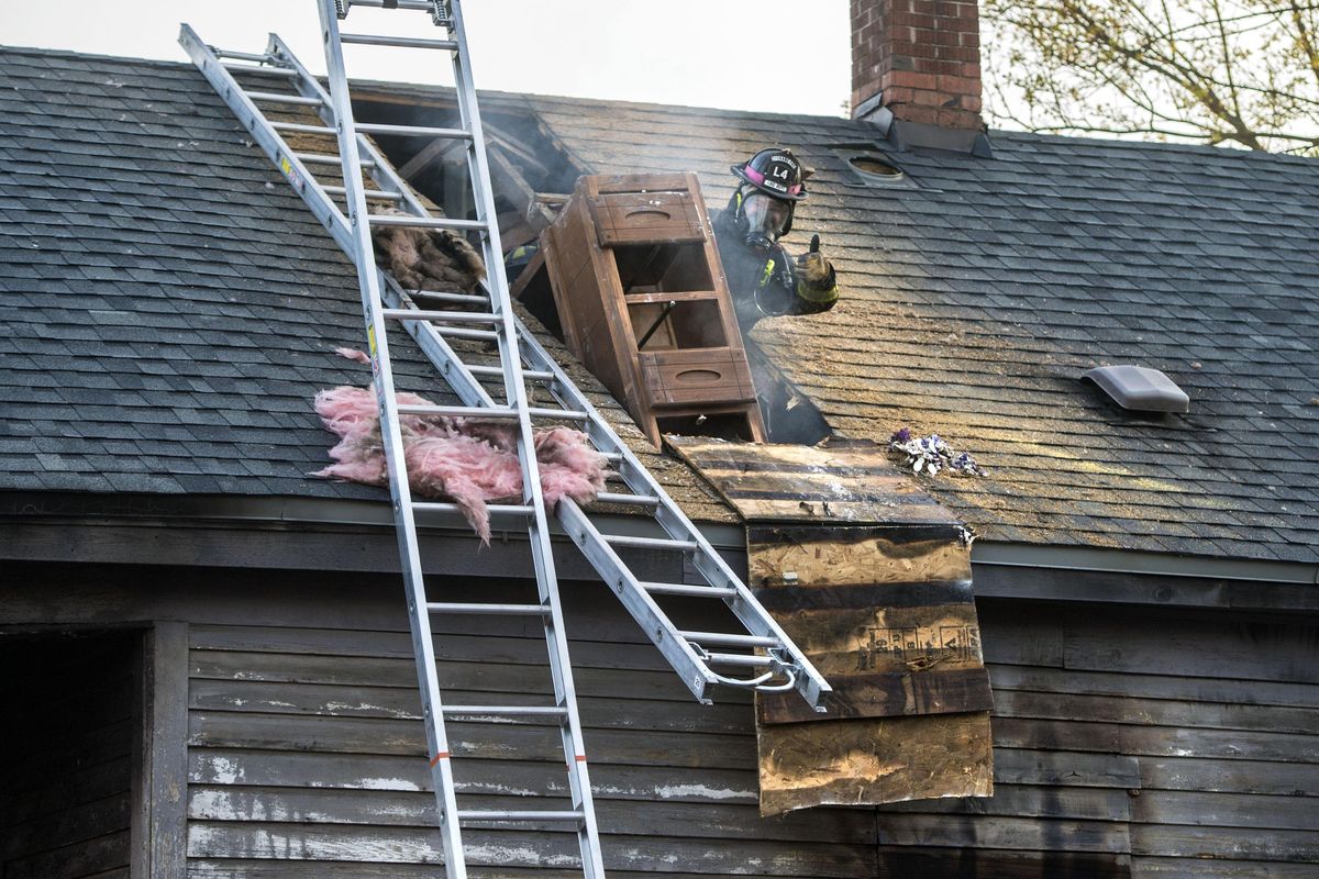 A Spokane firefighter checks with observers on the ground before tossing furniture out the roof of a house fire, April 19, 2017, at 117 S. Perry St., in Spokane, Wash. The early Wednesday morning fire is under investigation. (Dan Pelle / The Spokesman-Review)