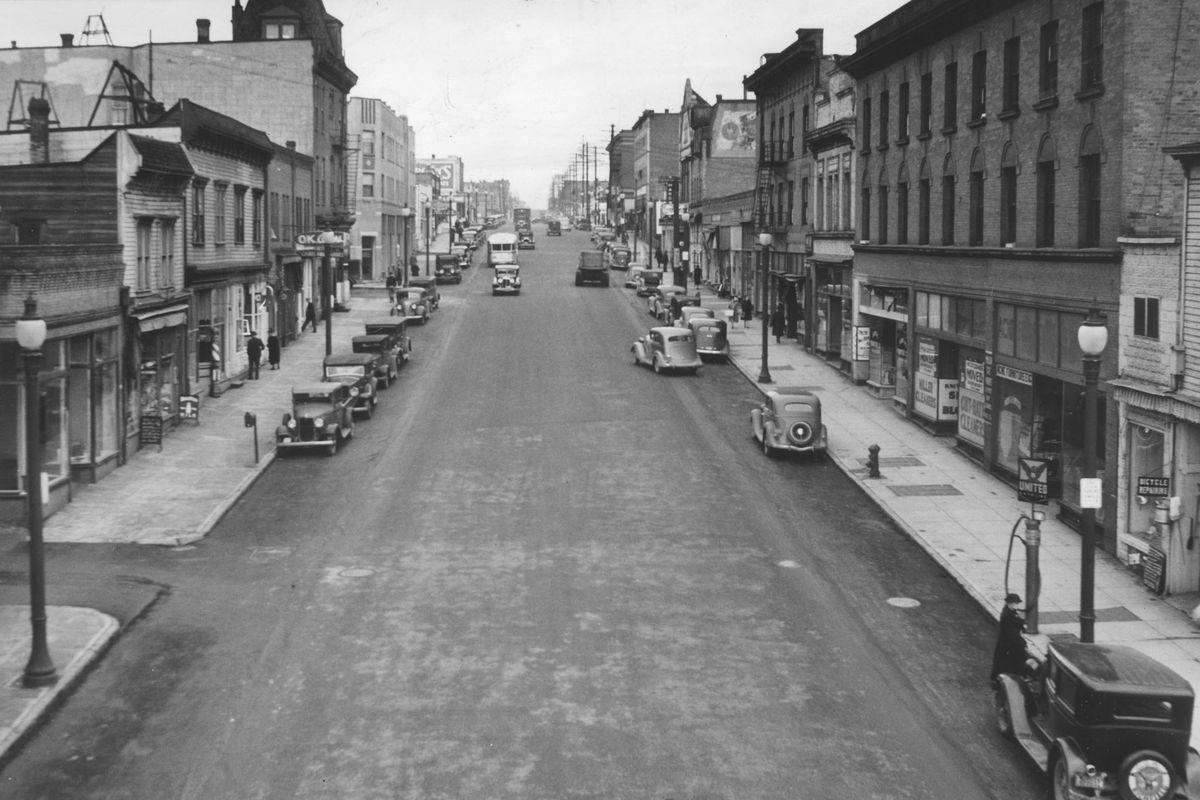 1937: Monroe Street is pictured just north of the bridge. Thielman Locksmith and the O.K. Cigar Store are on the left, and Acme Furniture and Miller Cleaners are on the right.