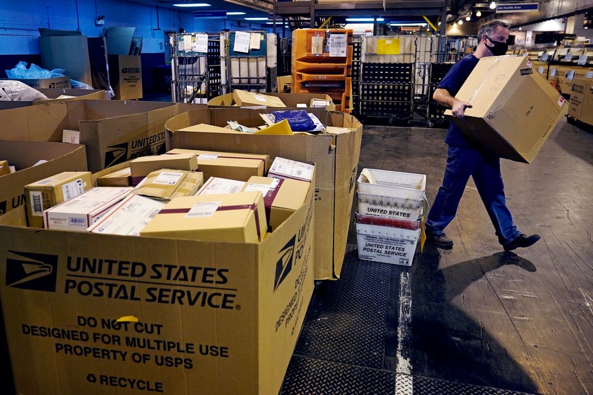 FILE - A worker carries a large parcel at the United States Postal Service sorting and processing facility Nov. 18, 2021, in Boston. Congress would lift onerous budget requirements that have helped push the Postal Service deeply into debt and would require it to continue delivering mail six days per week under bipartisan legislation that approached House approval Tuesday, Feb. 8, 2022. (Charles Krupa)