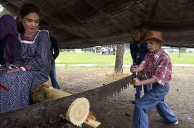 
Brooke Litalien, left, sits on a log to steady it and watches Andy Seib, right, try to saw through it with a double bucksaw Thursday during a gathering of mountain men, cowboys and military re-enactors who taught Ponderosa Elementary students about life in the West in the 1800s. The fourth graders learned to cook food in Dutch ovens, use a double bucksaw, viewed primitive medical instruments, and learned about life at Fort Spokane and Fort Sherman and guns of the old West. Behind Seib is librarian Nancy Haas. 
 (Photos by Jesse Tinsley/ / The Spokesman-Review)
