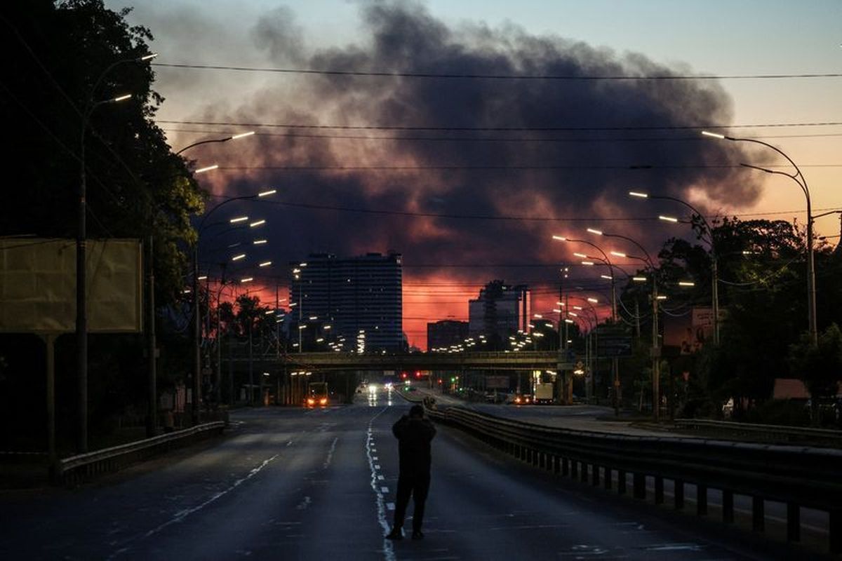 A man takes a picture of a street as smoke rises in the background after an overnight Russian missile and drone strike, amid Russia
