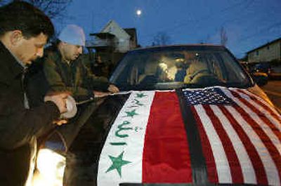 
Ali Al-Awadi, left, and Ali Al-Garawi tape Iraqi and U.S. flags to the hood of a van  in Seattle. About a dozen vans filled with Northwest-area Iraqis left Friday to make the trip to Los Angeles to vote in the Iraqi election. 
 (Associated Press / The Spokesman-Review)