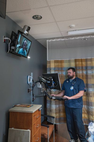 Josh Patterson, a registered nurse at St. Luke’s Health System, looks at a computer in a patient’s room in Nampa. Dr. Eric Rich appears on the other screen.  (St. Luke's Health System)