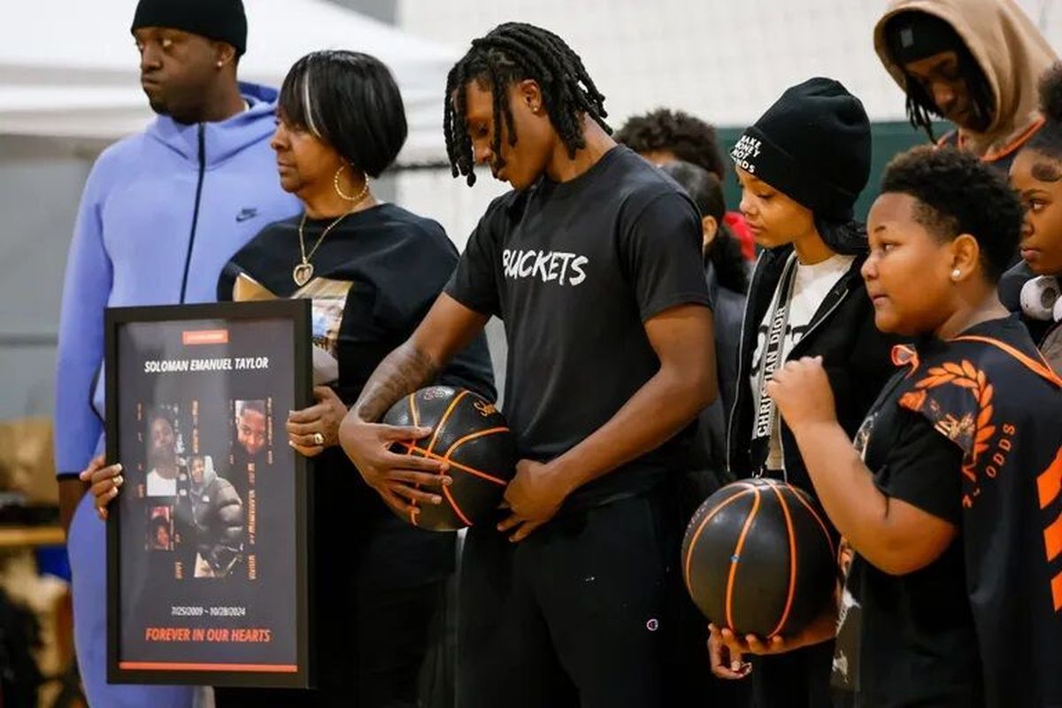 Samuel Taylor, surrounded by family, looks down at the basketball that holds the name of his brother, Soloman, at Hoop to Heal on Tuesday night in Kent. Soloman Taylor was 15 when he was shot and killed in October.  (Jennifer Buchanan/Seattle Times)