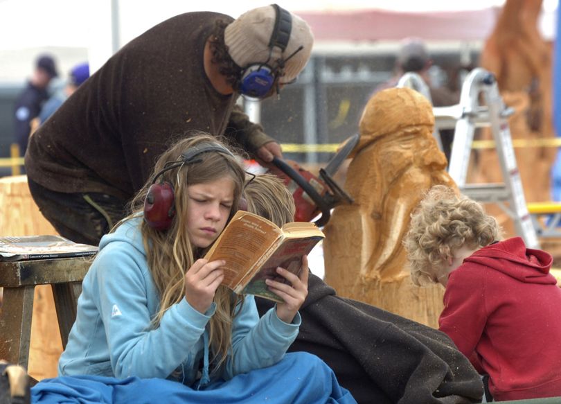 Ann Vreys, 13, concentrates on a book as she sits with her younger siblings while her father Luc Vreys, participates in a quick carve chainsaw competition during the Loggerodeo celebration in Sedro-Woolley, Wash. The Vreys family recently moved to Canada from Hechtel-Eksel Limburg, Belgium. Loggerodeo is Sedo-Woolley's Fourth of July celebration, featuring chainsaws carvers this weekend and a grand parade, footrace and rodeo on Sunday. (Scott Terrell / Skagit Valley Herald)