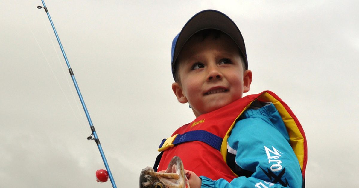 Boy carrying fishing pole by lake stock photo - OFFSET