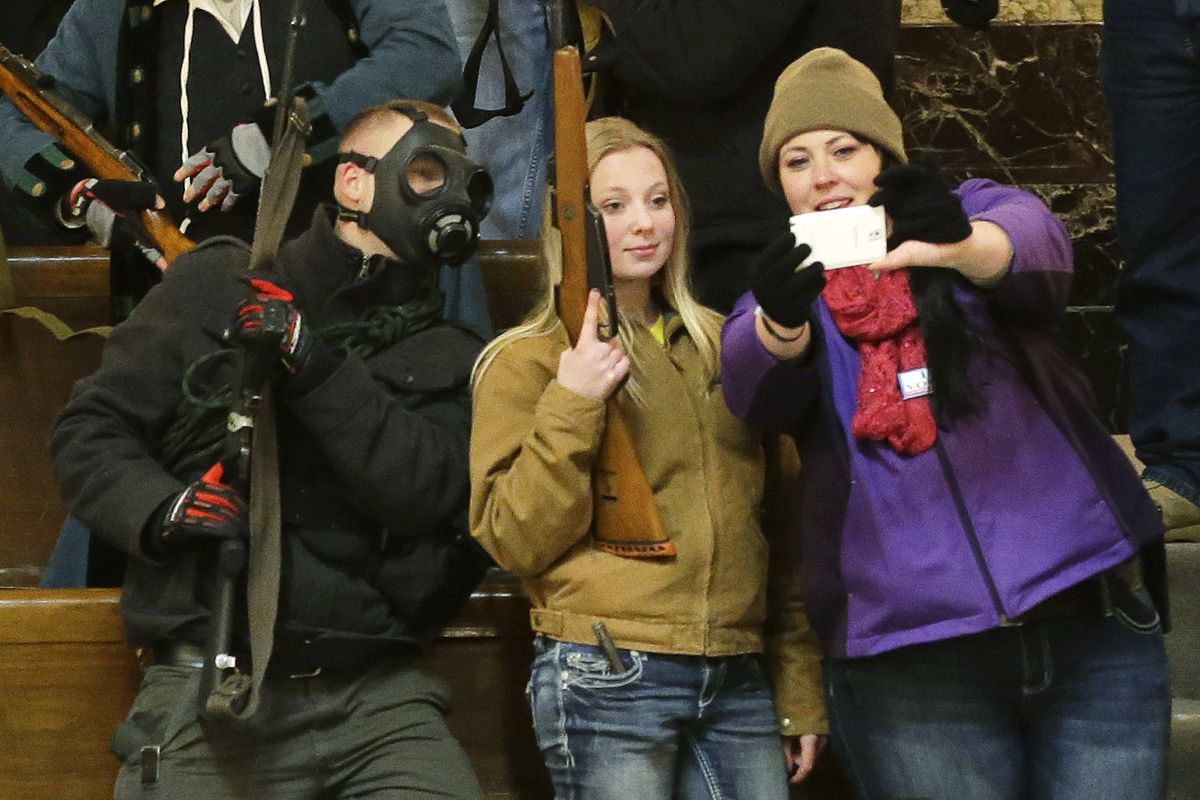 Gun owners, including Garrett Bosworth, 16, center, of Yakima, pose for a selfie photo as they display their weapons in the upper gallery of the House chambers Thursday at the Capitol in Olympia. The House was not in session when this photo was taken, and members of the group went to the gallery following a protest outside the legislative building in opposition to Initiative 594, which requires – with only a few exceptions – background checks on all gun sales and transfers. (Associated Press)