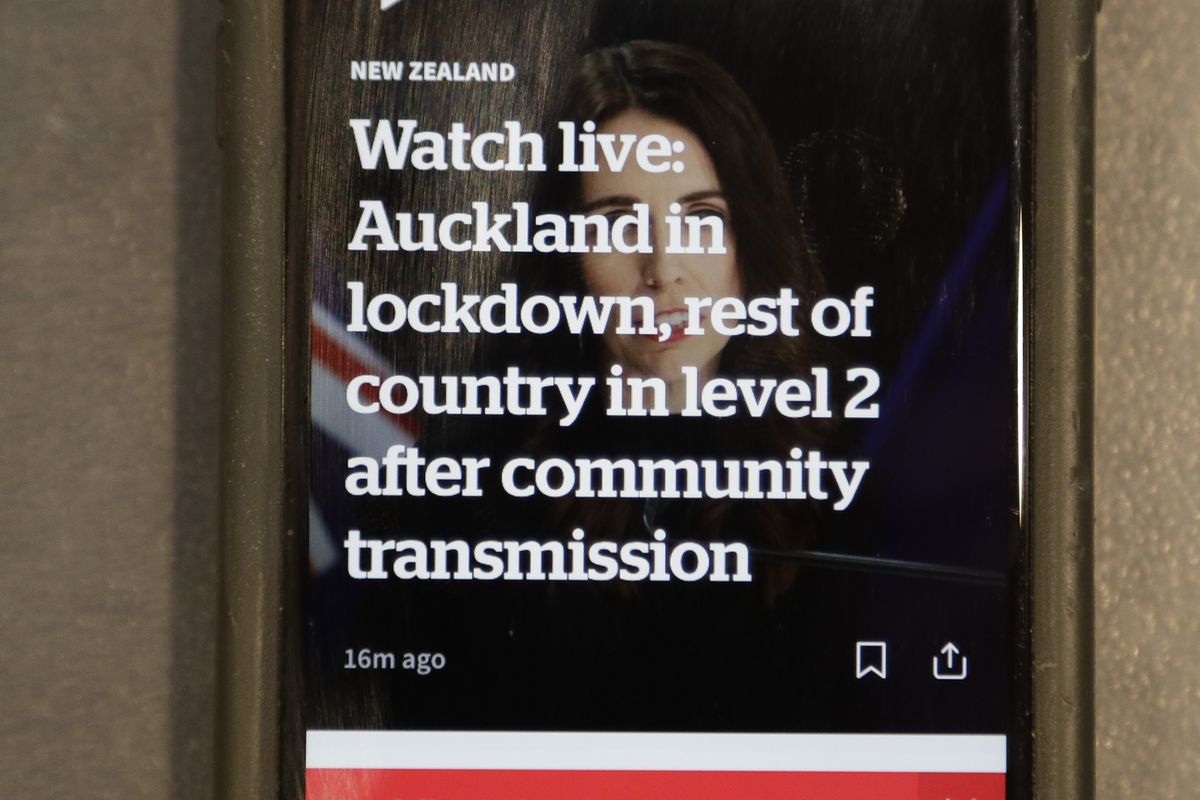 A news alert is displayed on a mobile phone in Christchurch, New Zealand, Tuesday, Aug. 11, 2020. New Zealand Prime Minister Jacinda Ardern said Tuesday that authorities have found four cases of the coronavirus in one Auckland household from an unknown source, the first cases of local transmission in the country in 102 days.  (Mark Baker)