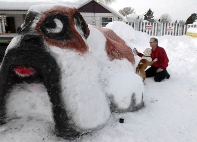 Snow sculptor Michael Ankney, right, adds color to his giant bulldog sculpture while Harley the bulldog hops on his lap outside Bulldog Towing in Hillyard on Tuesday. Rodney Stankey, owner of the towing company, asked Ankney to turn his bounty of snow into a mascot.  (Jesse Tinsley / The Spokesman-Review)