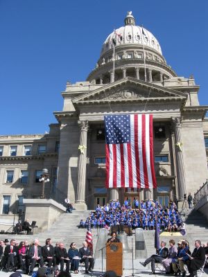 Idaho Sen. Cherie Buckner-Webb sings "America," as part of the state's celebration of its territorial sesquicentennial. Among those assembled are Gov. Butch Otter, at right, and at left, Abraham Lincoln portrayer Steve Holgate; further up the steps are the Horizon Explorers in Song, a group of more than 100 elementary school students who performed. (Betsy Russell)