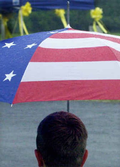 
Brayden Shinn sits in the rain under his flag-design umbrella, near a site decorated with yellow ribbons for a vigil for Paul Johnson Jr. in Eagleswood Township, N.J., Johnson's hometown. 
 (Associated Press / The Spokesman-Review)