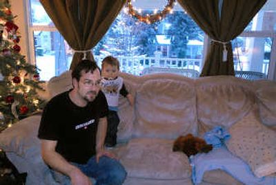 
John Hoffman sits with his 21-month-old son, Johnathan, at his South Hill home.  In August,  he found neighbor Jill Stuart's home (seen through the window, across the street) on fire and put it out with a fire extinguisher and a hose. His father-in-law helped him rescue Stuart's two dogs. 
 (Jesse Tinsley / The Spokesman-Review)
