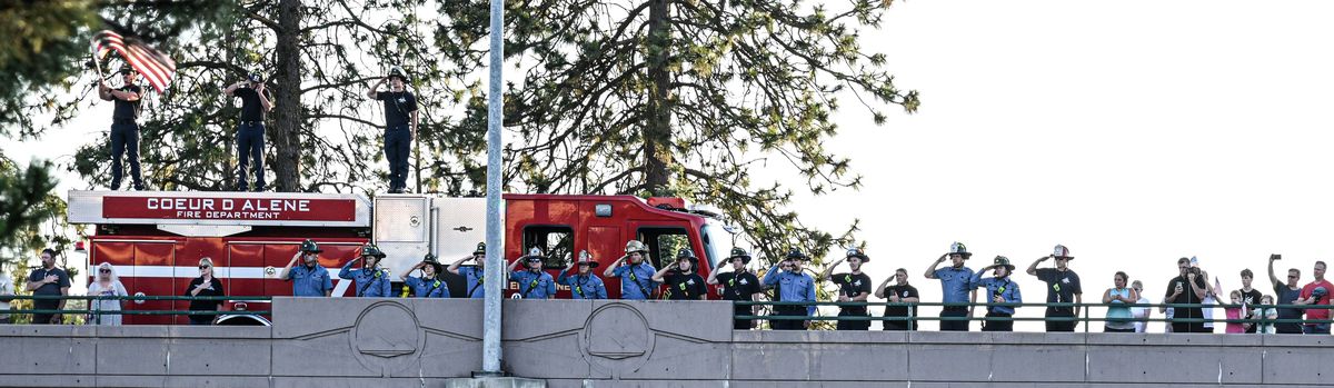 Firefighters and members of the community line the Northwest Blvd overpass during the procession for the two firefighters that were killed in an “ambush-style” attack in Coeur d