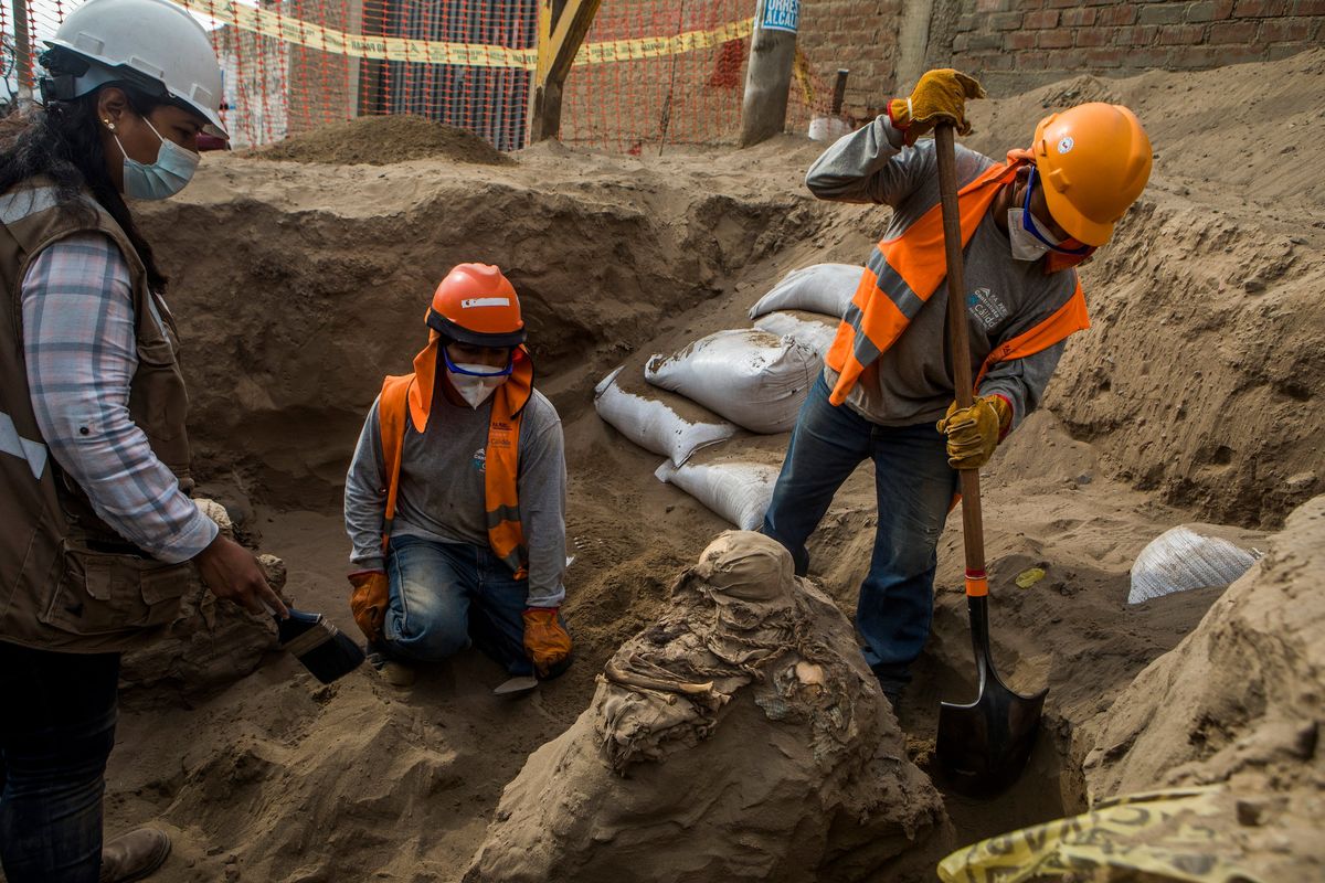 **EMBARGO: No electronic distribution, Web posting or street sales before TUESDAY 3:01 A.M. ET OCT. 11, 2022. No exceptions for any reasons. EMBARGO set by source.** Carlos Lalangui, right, digs around the remains of a funerary bundle in an ancient tomb discovered beneath a street in a residential district north of Lima, Peru, Sept. 30, 2022. In Lima, home to 10 million Peruvians and more than 1,000 archaeological sites, the discovery of an ancient tomb is just the latest encounter with an omnipresent past. (Marco Garro/The New York Times)  (MARCO GARRO)