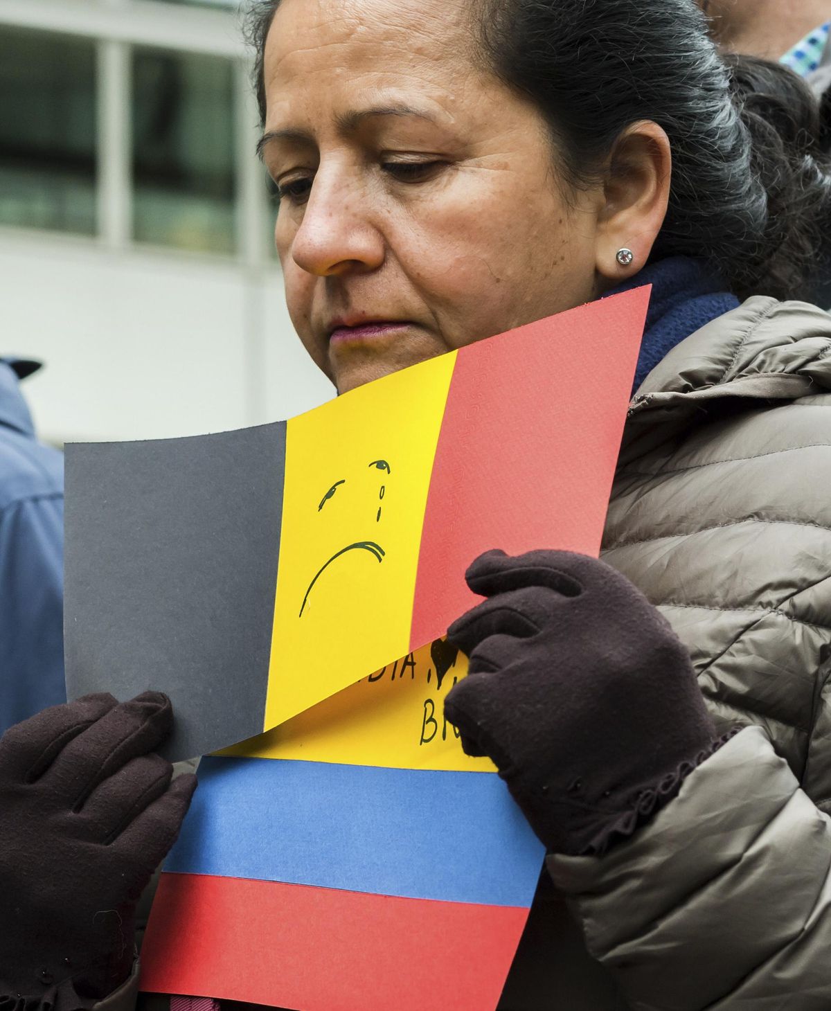 A woman holds a paper Belgian flag with a sad face on it as she participates in a minute of silence outside EU headquarters in Brussels on Wednesday, March 23, 2016. Belgian authorities were searching Wednesday for a top suspect in the country