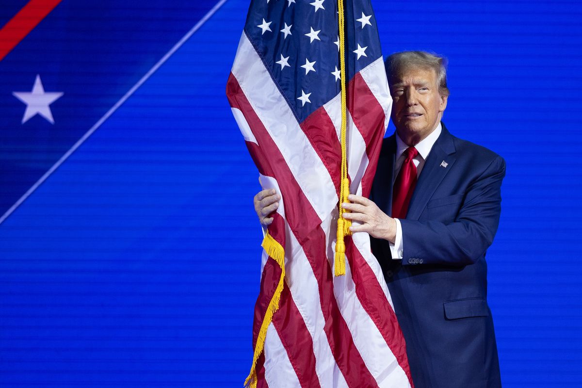 President Donald Trump hugs the American flag while walking onstage in 2024 in National Harbor, Maryland.   (Tom Brenner/For the Washington Post)